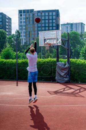 Foto de Jugador de baloncesto de hombre alto lanza una pelota en un aro de baloncesto en una cancha de baloncesto en el parque durante la práctica - Imagen libre de derechos