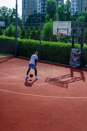 Photo for Tall guy basketball player with the ball shows his dribbling skills during practice on the basketball court in the park - Royalty Free Image