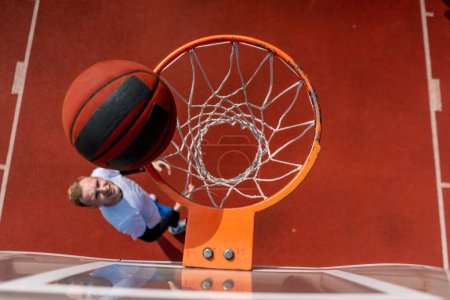 Téléchargez les photos : Gros plan de l'anneau de basket-ball dans lequel un grand joueur de basket-ball jette la balle d'en bas le concept d'admirer le jeu de basket-ball - en image libre de droit