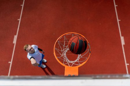 Foto de Primer plano del anillo de baloncesto en el que un jugador de baloncesto de hombre alto lanza la pelota desde abajo el concepto de admirar el juego de baloncesto - Imagen libre de derechos