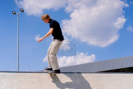 Photo for A young guy skater does a stunt on the edge of a skatepool against a backdrop of sky and clouds at city skate park - Royalty Free Image