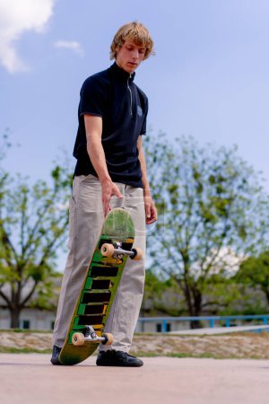 Téléchargez les photos : Un jeune skateboarder se tient dans un skatepark avec du skateboard à la main avant de commencer le skateboard - en image libre de droit