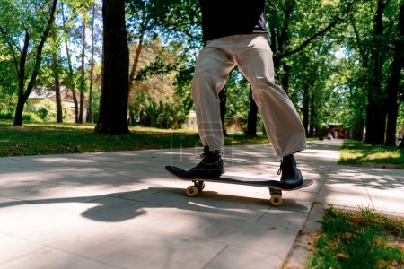 Foto de Primer plano de un niño haciendo un truco de skate en el camino del parque de la ciudad contra el fondo de los árboles - Imagen libre de derechos