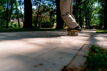 Photo for Young guy skater rides skateboard on the path of the city park against the background of trees and sky close-up - Royalty Free Image