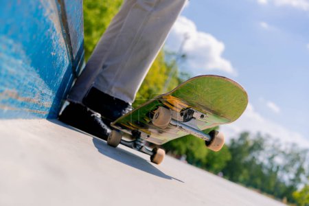 Foto de Primer plano de las piernas de un patinador con un monopatín mientras descansa entre trucos en el parque de skate de la ciudad - Imagen libre de derechos