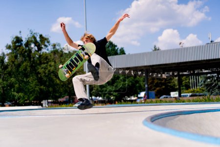 Foto de Un patinador joven cae mientras realiza una acrobacia en el borde de una piscina de skate contra el cielo y las nubes en el parque de skate de la ciudad - Imagen libre de derechos