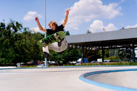 Ein kleiner Junge Skater fällt bei einem Stunt am Rande eines Skatepools gegen Himmel und Wolken im städtischen Skatepark