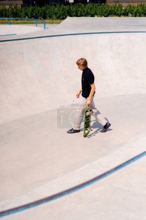 Foto de Joven skateboarder con el skate de pelo largo y haciendo trucos en la piscina de skate en el parque de skate de la ciudad - Imagen libre de derechos