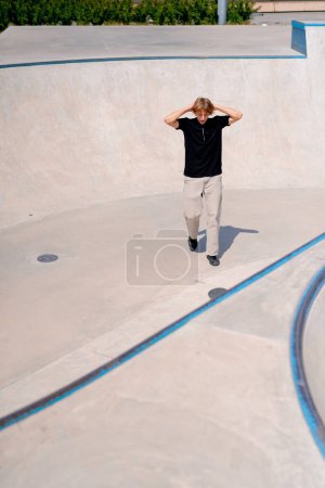 Téléchargez les photos : Un jeune skateboarder aux cheveux longs est skateboard et est contrarié par une cascade ratée à la piscine de skate au skatepark de la ville - en image libre de droit