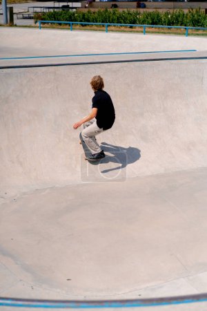 Téléchargez les photos : Jeune skateboarder avec des cheveux longs skateboard et faire des tours dans la piscine de skate au skatepark de la ville - en image libre de droit