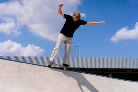 Foto de Un joven patinador hace un truco en el borde de una piscina de skate contra un telón de fondo de cielo y nubes en el parque de skate de la ciudad - Imagen libre de derechos
