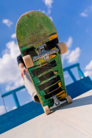 Téléchargez les photos : Gros plan d'une planche à roulettes tenue par le pied d'un jeune skateur dans un skatepark de la ville - en image libre de droit