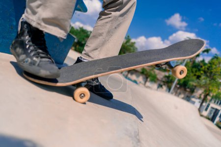 Photo for Close-up of a skateboard being held by the foot of a young skateboarder in city skatepark - Royalty Free Image