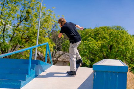 Photo for Young guy skateboarder with long hair skateboarding in the city skatepark and talking on the phone - Royalty Free Image