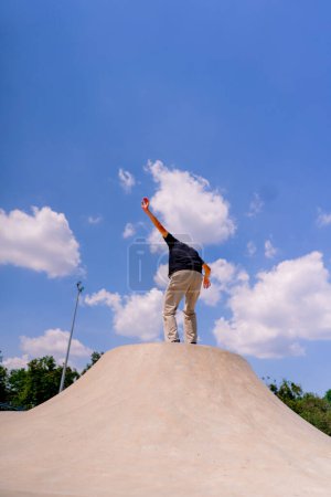 Téléchargez les photos : Un jeune patineur fait une cascade sur le bord d'une patinoire dans un contexte de ciel et de nuages au skate park de la ville - en image libre de droit