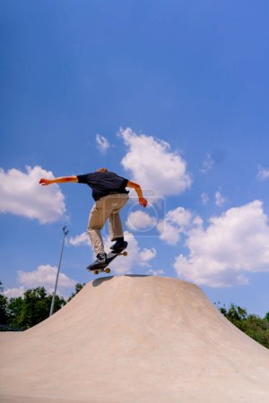 Téléchargez les photos : Un jeune patineur fait une cascade sur le bord d'une patinoire dans un contexte de ciel et de nuages au skate park de la ville - en image libre de droit