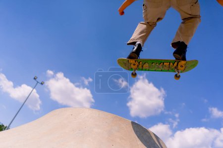 Photo for A young guy skater does a stunt on the edge of a skatepool against a backdrop of sky and clouds at city skate park - Royalty Free Image