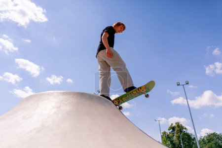 Photo for A young guy skater stands on the edge of a skate pool against a backdrop of sky and clouds at city skatepark - Royalty Free Image