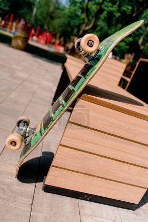 Téléchargez les photos : Gros plan d'une planche à roulettes debout à côté du banc dans le parc le concept de l'adrénaline envie et l'amour pour le skateboard - en image libre de droit