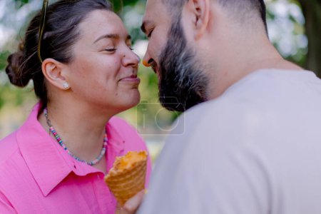 Foto de Joven pareja chico besos chica que está sosteniendo un helado en su mano durante la fecha en el parque - Imagen libre de derechos