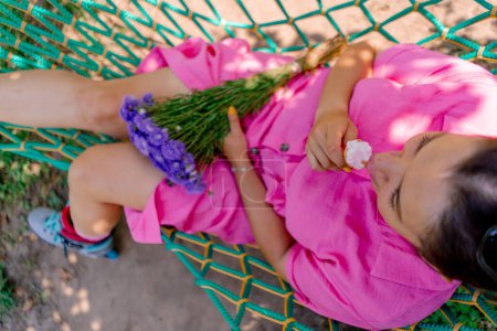 Téléchargez les photos : Jeune fille couchée sur un hamac dans le parc se reposant de roller et manger de la crème glacée - en image libre de droit