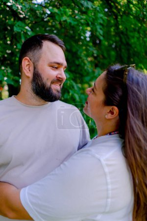 Foto de Retrato de una joven pareja de un hombre y una mujer de pie en un abrazo y besándose durante una cita en el fondo del parque modelo de tamaño más - Imagen libre de derechos