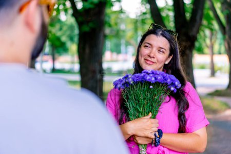Foto de Joven pareja hombre da ramo de flores a la chica en el parque y ella está feliz por ello - Imagen libre de derechos