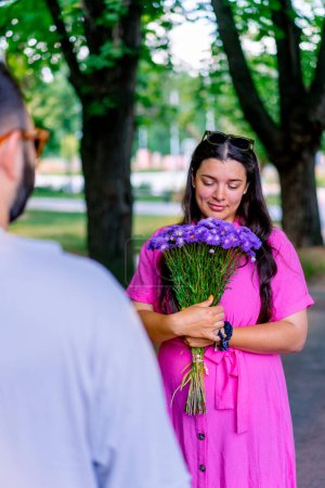 Foto de Joven pareja hombre da ramo de flores a la chica en el parque y ella está feliz por ello - Imagen libre de derechos