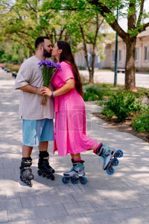 Téléchargez les photos : Jeune couple sur patins à roulettes gars donne fille un bouquet de fleurs pendant la date dans le parc - en image libre de droit
