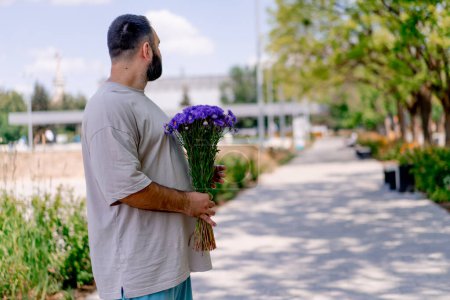 Téléchargez les photos : Guy sur patins à roulettes avec un bouquet de fleurs dans ses mains attendant dans le parc pour un concept de date fille dans le parc - en image libre de droit