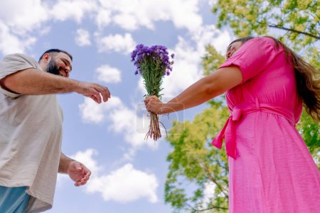 Téléchargez les photos : Jeune couple homme donne fille un bouquet de fleurs pendant la date sur rollers dans le parc - en image libre de droit