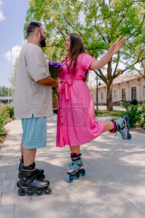 Foto de Joven pareja hombre da a chica un ramo de flores durante la fecha en patines en el parque - Imagen libre de derechos