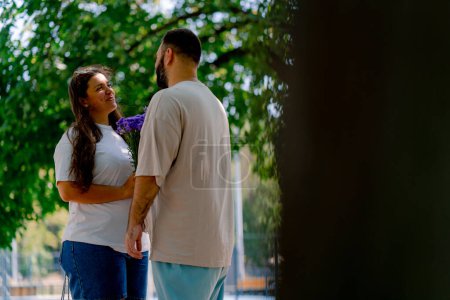 Photo for Young couple cheerful guy giving flowers to girl in park during date against background of trees plus size models - Royalty Free Image