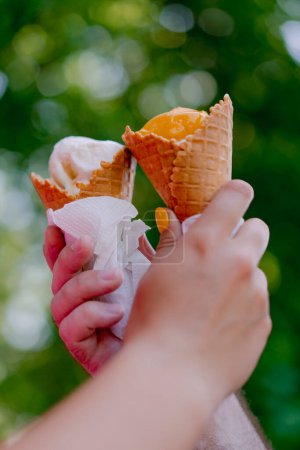 Photo for Close-up of guy and a girl holding ice cream with their hands during a romantic date in the park against the background of trees - Royalty Free Image