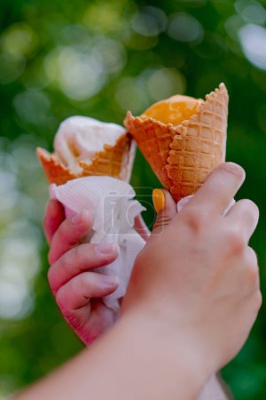 Foto de Primer plano del chico y una chica sosteniendo helado con sus manos durante una cita romántica en el parque contra el fondo de los árboles - Imagen libre de derechos