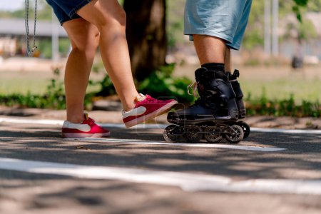 Téléchargez les photos : Jeune fille couple tient la main du gars qui est le patinage à roulettes et l'aide à apprendre à patiner dans le parc modèles plus de taille - en image libre de droit