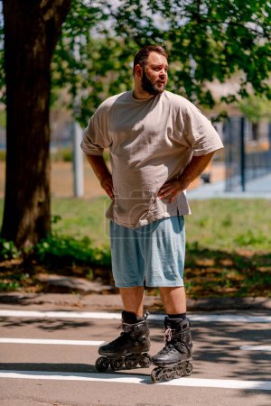 Photo for Portrait of young guy tired of rollerblading against the background of trees in the park plus sized model - Royalty Free Image