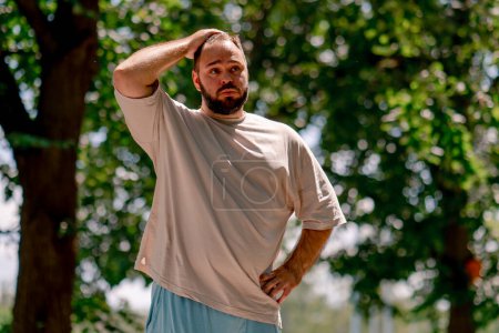 Photo for Portrait of young guy tired of rollerblading against the background of trees in the park plus sized model - Royalty Free Image