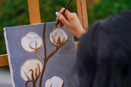 Téléchargez les photos : Une jeune fille artiste peint le tableau avec un pinceau sur une toile qui se dresse sur un chevalet vue de derrière le dos - en image libre de droit