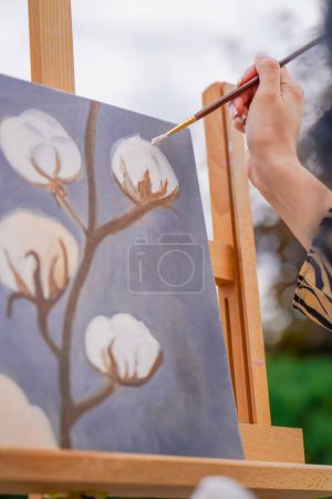 Foto de Una joven artista pinta un cuadro con un pincel sobre un lienzo que se levanta sobre una vista de caballete desde atrás - Imagen libre de derechos