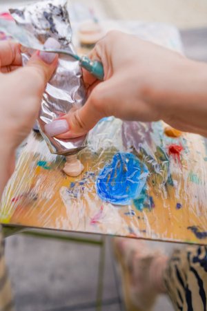 Téléchargez les photos : Gros plan d'une fille artiste pressant de la peinture d'un tube sur une palette en train de créer de la peinture - en image libre de droit