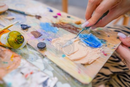 Téléchargez les photos : Gros plan d'une fille artiste utilisant une spatule de peinture pour prendre de la peinture d'une palette en cours de création - en image libre de droit