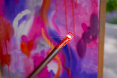 Téléchargez les photos : Gros plan d'une fille artiste avec un pinceau appliquant de la peinture à l'huile sur une peinture debout sur un chevalet dans un studio de peinture - en image libre de droit