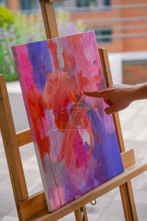 Foto de Primer plano de una artista con su dedo aplicando pintura al óleo a una pintura de pie sobre un caballete en el estudio de pintura - Imagen libre de derechos