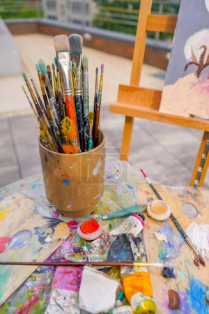 Photo for Close-up of a painting stand with paint brushes against the street and painting on an easel - Royalty Free Image