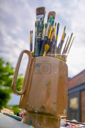 Foto de Primer plano de un soporte de pintura con pinceles contra la calle y pintura sobre un caballete - Imagen libre de derechos