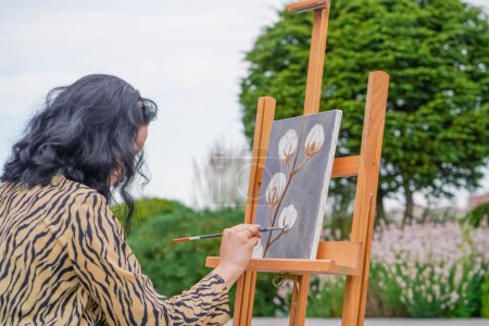 Foto de Una joven artista pinta un cuadro con un pincel sobre un lienzo que se levanta sobre una vista de caballete desde atrás - Imagen libre de derechos