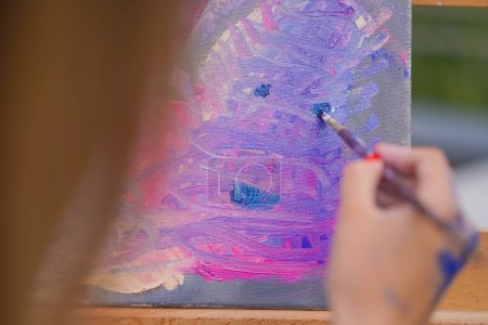 Photo for A young girl artist paints picture with a brush on a canvas that stands on an easel view from behind the back - Royalty Free Image