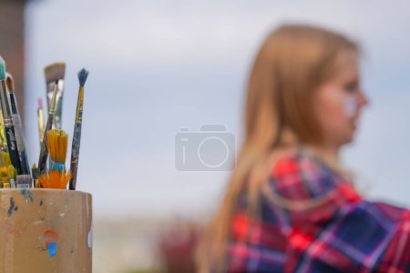 Photo for Close-up of a painting stand with paint brushes against the street and painting on an easel - Royalty Free Image