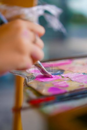 Téléchargez les photos : Gros plan d'une fille artiste assise près d'un chevalet et prenant la peinture d'une palette avec un pinceau le concept d'amour des beaux-arts - en image libre de droit